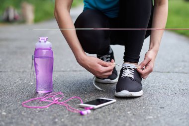 Koşu ayakkabısı bağlayan koşucu kadın koşuya hazırlanıyor stadyumda bir şişe su ve kulaklıkla koşuya hazırlanıyor.