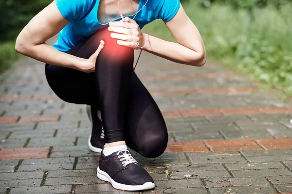Kadın atlet, dizine acı içinde dokunuyor, kadın sporcu yaz parkında koşuyor. Sağlıklı yaşam tarzı ve spor anlayışı.