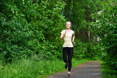 Genç fitness kadını orman yolunda koşuyor.