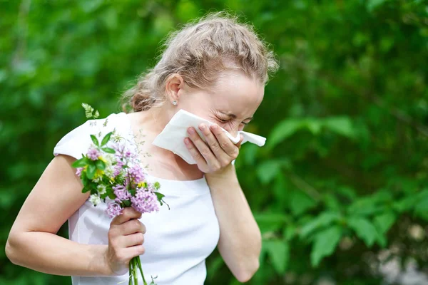Pollen allergy, girl sneezing with bouquet of flowers. Concept: seasonal allergy.