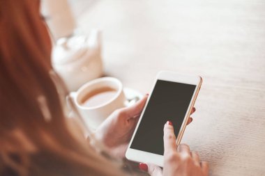 Akıllı telefonları, kulaklıkları ve bir fincan çayı olan kadın elleri. Grafik görüntüleme montajı için