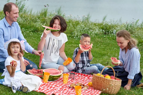 Mutlu aile piknikte karpuz yiyor. Genç arkadaşlar ve onların çocukları doğada — Stok fotoğraf