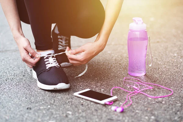 Koşu ayakkabısı bağlayan koşucu kadın koşuya hazırlanıyor stadyumda bir şişe su ve kulaklıkla koşuya hazırlanıyor.