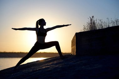 Siluet kadın yoga yapıyor ya da gün batımında ya da gün doğumunda sahilde geriniyor..