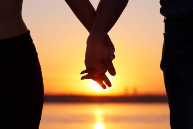 Sahilde el ele tutuşuyor. Gün doğumunda romantik sahnede ellerini tutan siluet çift