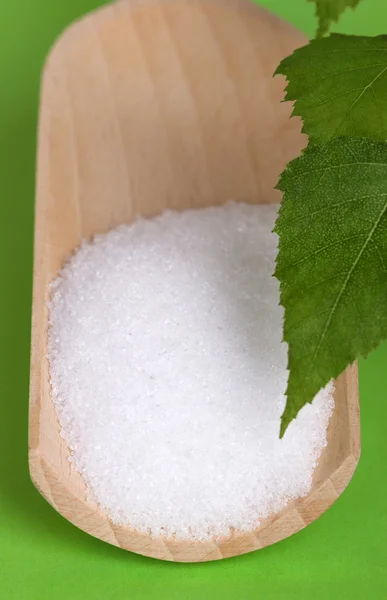 Xylitol açúcar de vidoeiro em colher de madeira sobre verde — Fotografia de Stock