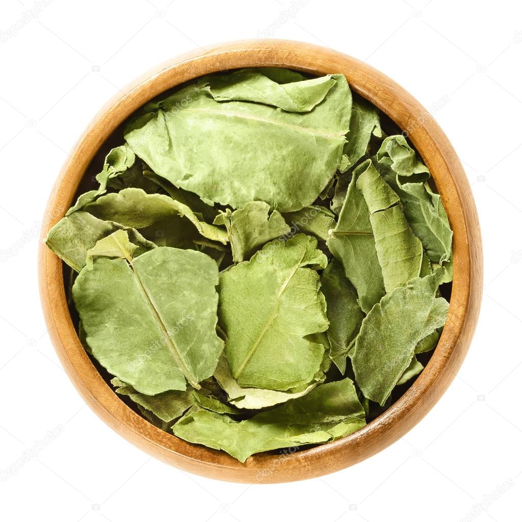 Dried kaffir lime leaves in wooden bowl over white