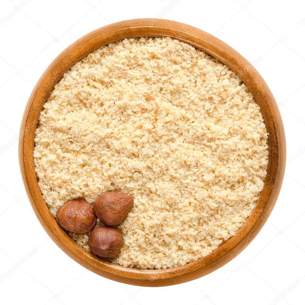 Three shelled hazelnuts on hazelnut meal in wooden bowl