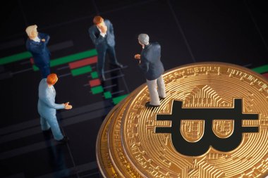 Makro minyatür işadamı figürü altın bitcoin yığınının üzerinde duruyor ve diğer iş adamlarıyla konuşuyor. Arkaplanda borsa grafikleri var. Geleceğin para birimi ve engel zinciri konseptiyle ilgili iş toplantısı.