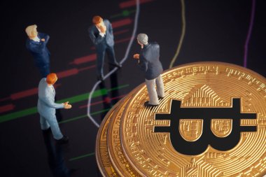 Makro minyatür işadamı figürü altın bitcoin yığınının üzerinde duruyor ve diğer iş adamlarıyla konuşuyor. Arkaplanda borsa grafikleri var. Geleceğin para birimi ve engel zinciri konseptiyle ilgili iş toplantısı.