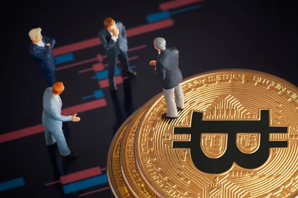 Makro minyatür işadamı figürü altın bitcoin yığınının üzerinde duruyor ve diğer iş adamlarıyla konuşuyor. Arkaplanda borsa grafikleri var. Geleceğin para birimi ve engel zinciri konseptiyle ilgili iş toplantısı.