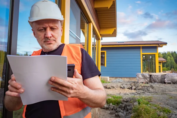 Building. Customer checks the estimate. Man checks documents at home. Man in a hard hat and construction vest. Builder looks at the plan for the upcoming work. Builder with papers in hands.