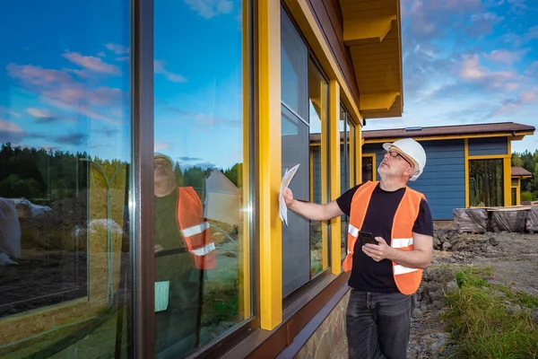 The engineer checks the quality of construction work. Assessment of the quality of installation of Windows in the cottage. The Builder calls the customer works. The firm is responsible for its work.