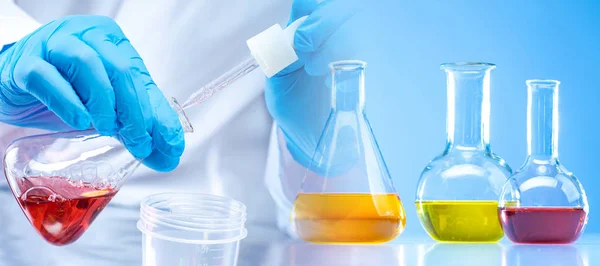 The hands of the chemist and chemical flasks with colored liquids. Demonstration of experiments in chemistry class. Development of new synthetic detergents. Analysis of raw materials for production.