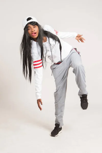A girl with black skin in a white cap poses in an unusual pose. Concepts of a teenager. Youth culture. Youth fashion. An African-American woman in a knitwear, cap, and sneakers.