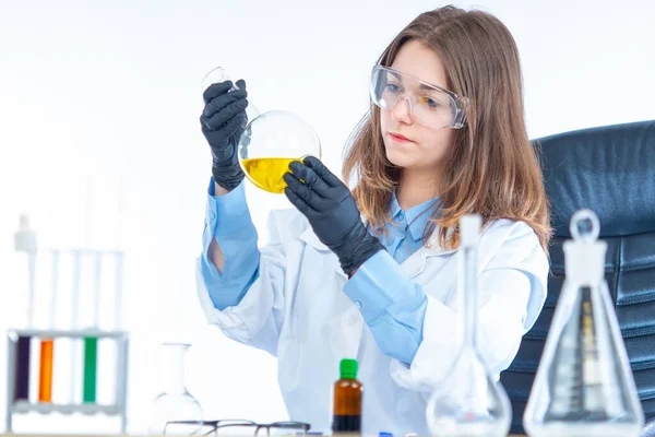 Girl in a medical laboratory. A medical worker makes a medicine. Pharmacologist in a medical laboratory. Young formate in safety glasses. Lab technician holding a large flask in his hands