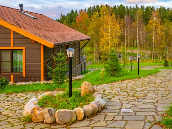 Country cottage. House near the forest. Wooden house in sunny weather. A stone walkway leads into the forest. Concept - sale of natural stone. Concept - landscape design. Summer holiday home