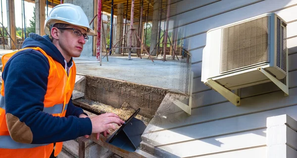 Builder with a tablet near a house under construction. Concept - an engineer thinks through communications. Concept - the builder is considering a place for installing an air conditioner.