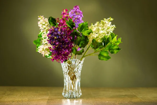 Lilac. Vase with colorful lilacs on a wooden table. Flowers in a crystal vase on a brown background. Flowering shrubs. Bouquet of lilacs in a vase on the table.