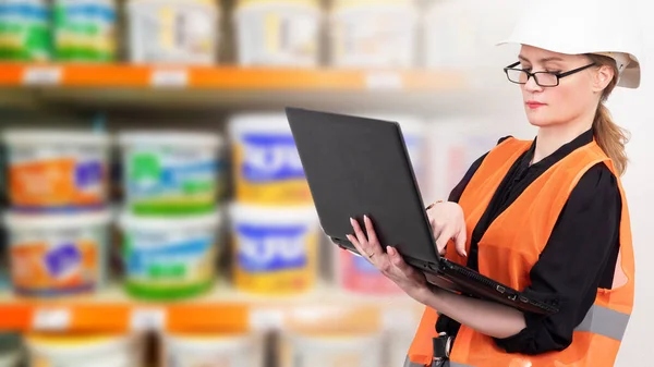 Woman with laptop on the background of store shelves. Concept - team leader in a hardware store. Purchase of building materials. Purchase of goods for building house. Woman in a building online store