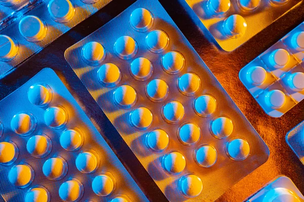 Blisters with pills close-up. Packets of pills on the brown table. Tablets in blue-yellow lighting. Pharmacological background. Treat disease. Development of new medicines. Pharmacy.
