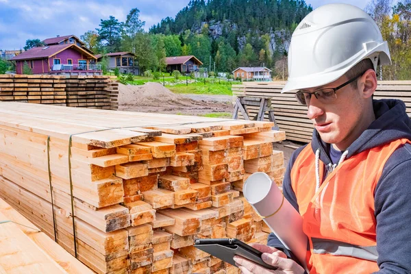 Builder on the site of the future home. Architect at the construction site. Concept - work in a construction company. A man with drawings and a tablet. Wooden beams prepared for construction.