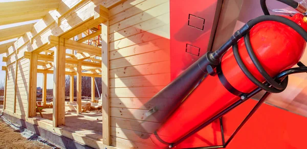 The frame of a house under construction and a fire extinguisher. Fire prevention on the construction site. Development of a fire safety project. Equipping a new house with extinguishing systems.