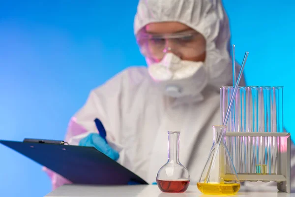 Chemist. Work in the laboratory. Lab technician records the results. Concept - hazardous chemicals. A man in a respirator in a laboratory. Safety when working with reagents. Laboratory research.