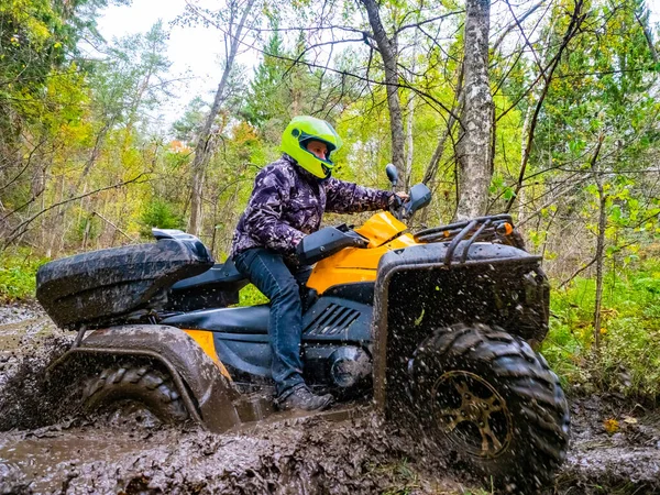 A man rides a ATV on a dirt road. Rider on a Quad bike in a puddle of mud. It is driving on a very muddy forest road. Extreme Quad bike riding. Off-road ATV racing.