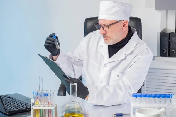 A doctor in a white coat and cap examines the substance in a plastic test tube. The person compares the substance in the flask with the test values. Medical test. Medical diagnostics.