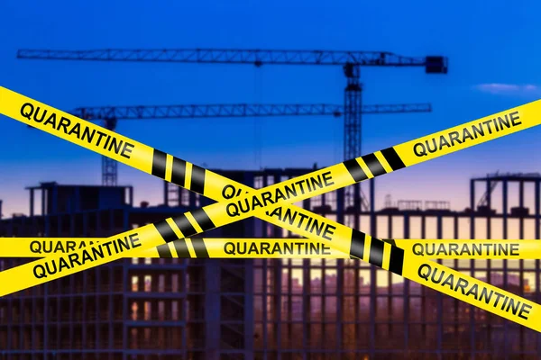 Construction of a multi-storey building is stopped. Freezing the construction of residential tasks. Building process is quarantined. Construction crane on background of the sky. Fever Warning tape.