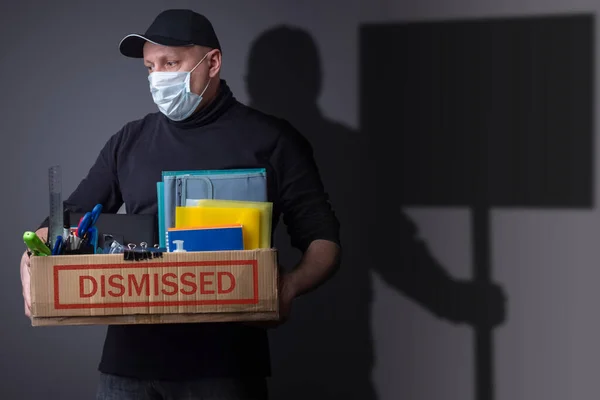 A fired employee in a medical mask and his shadow with a poster. Social tension due to unemployment. Strikes. Lack of livelihood. Lack of work. Collapse in the economy.