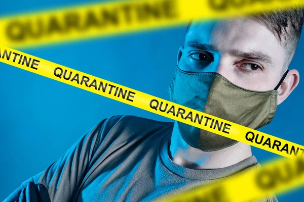 A sad man in a protective mask behind yellow ribbons with the words Quarantine. Self-isolation. Restrictions in connection with the epidemic of the coronavirus. Attempts to prevent the disease.