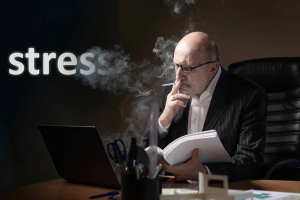 A man smokes in his office on the background of the inscription Stress. A person works hard. A large amount of work. Stress from work. Irregular working hours. Methods for dealing with stress.