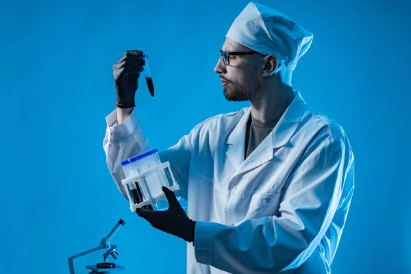 A laboratory assistant holds test tubes with blood samples. All types of laboratory tests. Research of biological fluids. Doctor with blood samples on a blue background. Laboratory diagnostics.