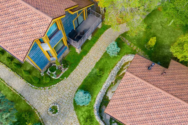 Territory of the house is a top view. Stone path between two houses. The territory of the cottage village is decorated with stone. Country houses made of wood. Roofs of cottages drone view