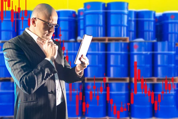 Man works as broker at the oil exchange. Concept - exchange cost of petroleum products. Schedule reduction on the background of barrels. Looks thoughtfully at tablet. Concept - oil prices stabilized