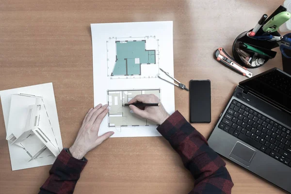 Architect works with drawings of a building. Man makes notes on a floor plan. Concept - hands of architect. Architect\'s desk top view. Concept - work in an architectural bureau. Layout of the house