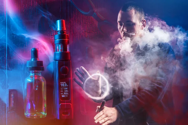 Vape. Vaper. Vaping. Smoking electronic cigarettes. Man in a couple clubs. Guy in the clouds of smoke. Concept - set for the vaper. Guy pokes a ring of smoke with his hand. Sale of oils for vaper.