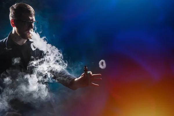 Vaper in puffs of smoke. Man and smoke on a dark background. Ring from an electronic cigarette. Concept - buying a devas for a vaper. The guy is vaping. Components and accessories for vape.