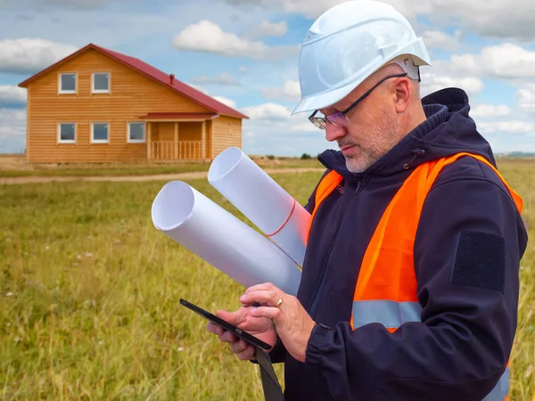 Builder at the site of future construction. Concept - builder away from the built house. Construction of country cottages. Concept - work in an architectural bureau. Man looks at the phone.