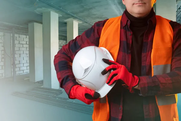 Man in a suit of builder. Concept - work as a blue collar. Concept - sale of building uniforms. White helmet in hands of builder. Work in the construction industry. Human in the newly built premises