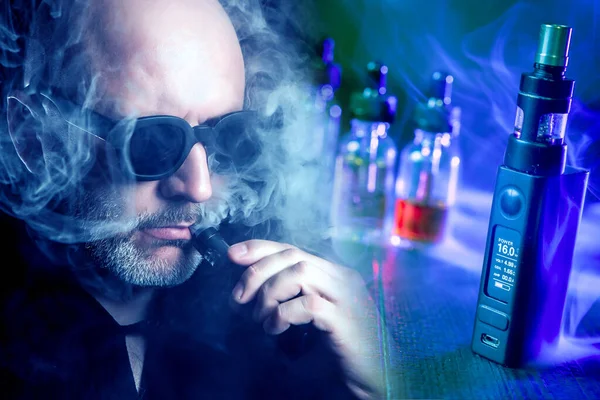 VAPE man. Portrait of a bearded man Smoking a VAPE. A man with black glasses lets out smoke from an e-cigarette. Smoker and devices for Smoking e-cigarettes.