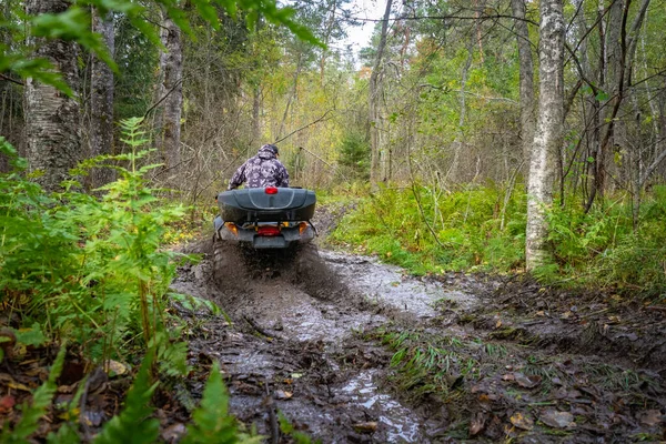 A man rides an ATV rear view. Riding an Quadrocycle through mud. Off-road travel. Concept is the lack of roads. Extreme sports. Concept - sale of ATVs and accessories. Quadrocycle stuck in the mud
