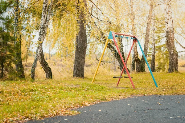 Дитячі гойдалки на залізних ланцюгах для їзди та розваг з жовтим листям на землі восени . — стокове фото