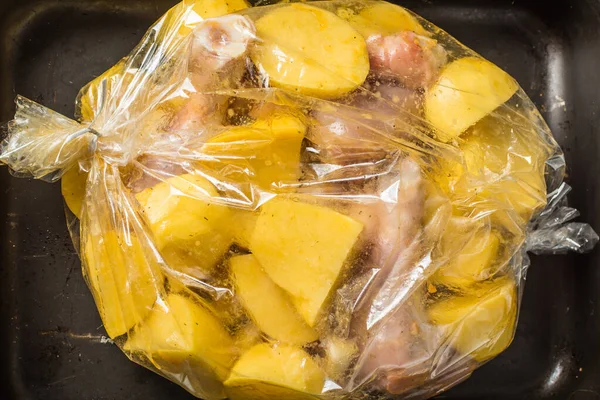 Raw chicken legs and sliced potatoes in roasting bag in oven. — Stock Photo, Image