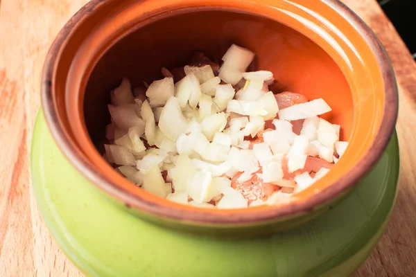 Rauwe gesneden kipfilet bestrooid met uien in een keramische pot voor het koken in de oven. — Stockfoto