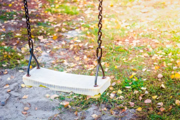 Childrens swing on iron chains for riding and entertainment with yellow foliage on ground in autumn day.