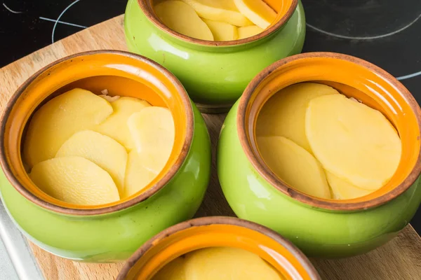 Patatas frescas en rodajas ponen en maceta de cerámica para cocinar en el horno . —  Fotos de Stock