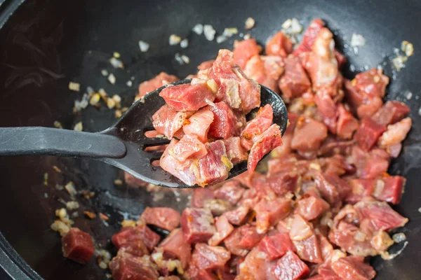 Appetizing pieces of red calf tenderloin with plastic spoon for mixing are fried in large cauldron for pilaf. — 스톡 사진